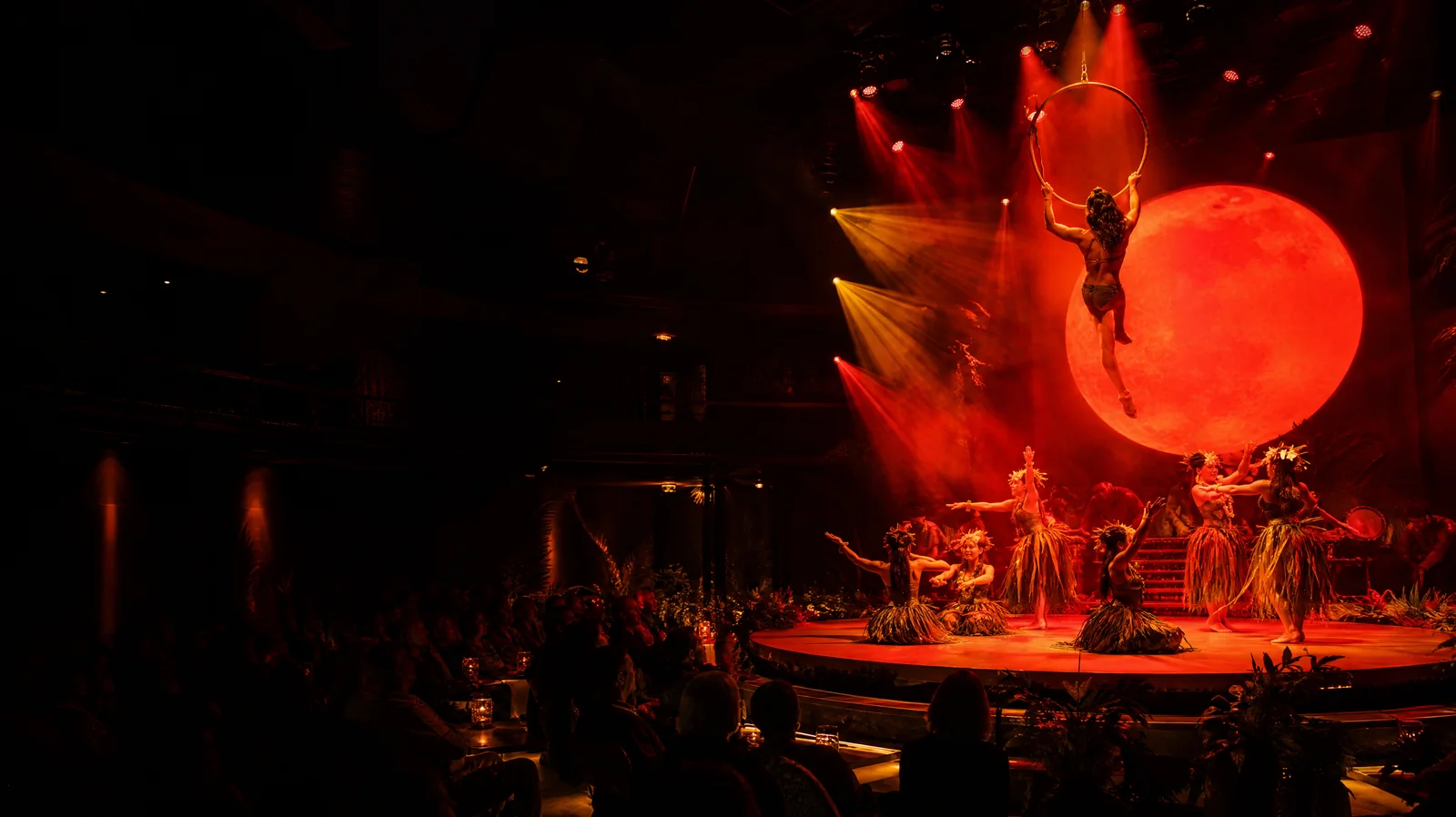 Aerialist on a golden hoop above a Hawaiian-themed circus stage in Waikiki